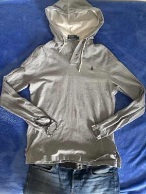 Grå Ralph lauren hoodie - Skick: 9/10, använd på ett mycket sparsamt sätt Defekter: inga, noll hål och inga fläckar Storlek: storleken är S men den är lite stor i storleken, så jag skulle rekommendera storlek M. Jag är 178 och väger 65kg, och jag tycker den är lite för stor runt ärmarna och på längden. Vid frågor eller funderingar är det bara att skicka. Priset är ej hugget i sten!😁