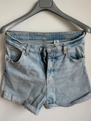 Högmidjade denimshorts från H&M (&Denim) - Modell: "Mom Shorts Ultra High Waist" från H&M (&Denim)  Färg: Ljusblå klassisk denimtvätt  Storlek: EUR 34 (US 2 / CA 2 / MX 2)  Skick: Mycket fint begagnat skick, inga synliga fläckar eller defekter  Detaljer: Hög midja, uppvikta benslut och klassisk femficksmodell  Rök- och djurfritt hem. Fraktar snabbt! ✨ 