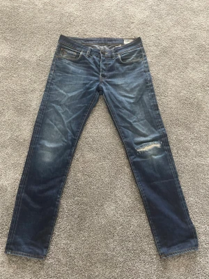 Blå raka jeans från G-Star RAW - Säljer ett par blå jeans från G-Star RAW, modell 3301. Jeansen har raka ben, klassisk femficksdesign och slitningar på höger knä för en cool, avslappnad look. Riktiga unika och schyssta fades på dessa jeans. Jeansen har en ny gylfknapp men borde inte vara något större besvär. Tveka inte på att höra av dig vid frågor eller fler bilder/mått W32 L32