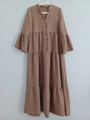 Khaki brown maxi dress  - Elegant khaki brown maxi dress with ruffle details and flared sleeves. Lightweight, flowy, non-stretch fabric with a loose and comfortable fit.  Size: S / 36 Condition: Very good — worn once indoors, when tried on. Colour: Khaki brown Material: Polyester  Measurements: • Length: 129 cm • Sleeve: 51 cm  Perfect for summer, holidays, dinners, weddings or other occasions.🤎
