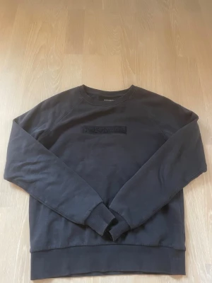 Svart sweatshirt Peak Performance XS - Mörkgrå/svart sweatshirt från Peak Performance i storlek XS. Klassisk modell med rund halsringning, ribbade muddar och diskret broderad logga på bröstet. Perfekt till jeans eller joggers för en clean och enkel look.