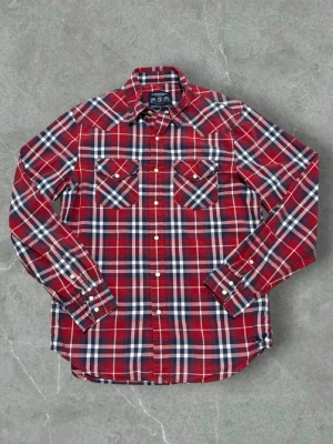 Röd rutig skjorta från American Eagle - Klassisk röd och blå rutig skjorta från American Eagle Outfitters i vintage fit. Skjortan har två bröstfickor med knappstängning, vita knappar och lång ärm. Perfekt för en avslappnad och stilren look. True to size! Bara att höra av sig kring minsta fundering🙌