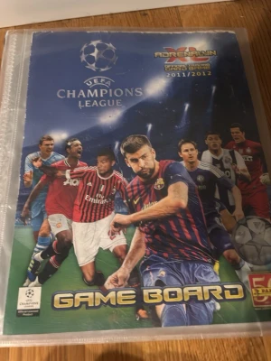 UEFA Champions League Adrenalyn XL pärm - Säljer en UEFA Champions League Adrenalyn XL Game Board-pärm från säsongen 2011/2012 med samlarkort. Pärmen är blå med fotbollsmotiv och innehåller flera fotbollskort, bland annat med spelare från Bayern München. Perfekt för samlare och fotbollsälskare.