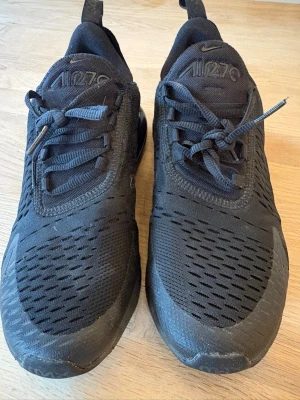 Nike Air Max 270 helsvarta sneakers - Säljer ett par helsvarta Nike Air Max 270 sneakers med mesh-överdel och synlig Air-enhet i hälen. Skorna har en sportig look med klassisk Nike-logga och snörning. Perfekta för dig som gillar stilrena och bekväma sneakers.