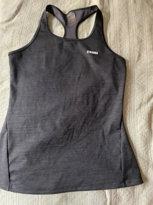 Grått träningslinne från Stronger - nytt, blev aldrig använt  - Snyggt grått träningslinne från Stronger med brottarrygg. Tillverkat i ett stretchigt material av 78% polyester och 22% elastan som andas bra under träningen. Perfekt för gymmet eller löprundan.