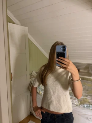 Beige stickad topp med kort ärm - Säljer en beige stickad topp med korta ärmar och hög hals. Toppen har en rak passform och är perfekt för dig som gillar en enkel men ändå stilren look. Materialet känns mjukt och bekvämt mot huden.