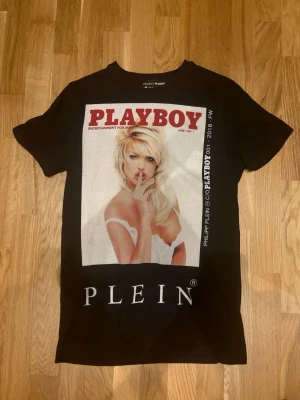 Svart Playboy x Plein t-shirt - Cool svart t-shirt från Philipp Plein med stor Playboy-tryck framtill. T-shirten har klassisk passform och är kortärmad. Materialet är mjuk bomull och trycket har en vintagekänsla med röd och vit text.