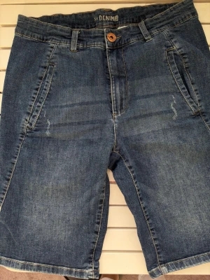 Blå denimshorts med fickor - Klassiska blå denimshorts med normal passform och fem fickor. Shortsen har bälteshällor, knappstängning och dragkedja framtill. Perfekta för varma dagar och har en tidlös look som passar till det mesta. Str 38