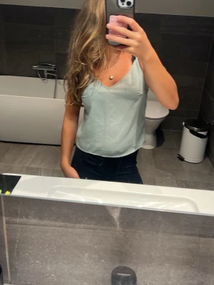 Ljusgrön linnetopp med smala band - Säljer en stilren ljusgrön linnetopp med smala axelband och v-ringning. Toppen har en enkel och clean look som passar perfekt till jeans eller kjol. Materialet känns lätt och svalt, perfekt för varmare dagar.