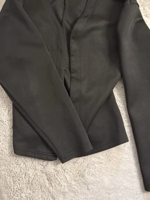 Svart långärmad topp från SHEIN - Snygg svart långärmad topp från SHEIN med figurnära passform. Tillverkad i ett mjukt och stretchigt syntetmaterial som känns bekvämt mot huden. Perfekt att styla med jeans eller kjol för en trendig look.