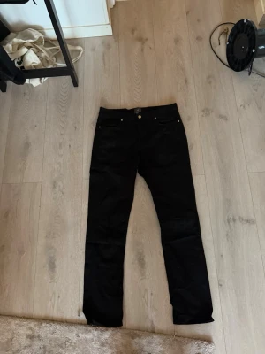 Svarta raka jeans - Säljer ett par svarta jeans med rak passform och klassisk femficksdesign. Jeansen har knappgylf och silverfärgade nitar. Perfekta till en avslappnad stil och funkar året runt.