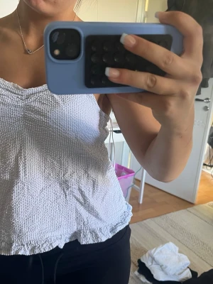 Gullig topp från Gina  - Säljer en söt vit linnetopp med smockad struktur och tunna axelband. Toppen har volangkant nedtill och är perfekt för varma dagar. Enkel och stilren design som passar till det mesta. Perfekt under en tjockare tröja