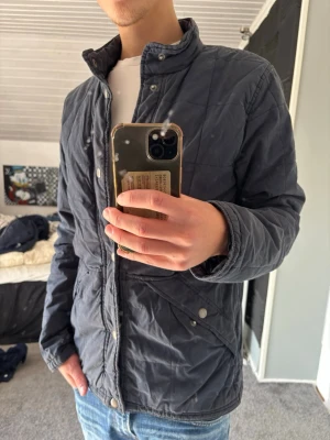 Abercrombie & Fitch jacka - Snygg mörkblå quiltad jacka med hög krage och tryckknappar framtill. Jackan har lång ärm och två snedställda fickor med knappstängning. Perfekt för kyligare dagar och ger en clean look till din outfit.