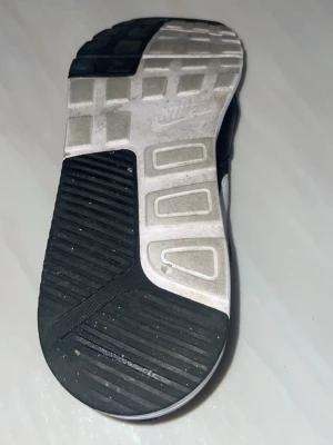 Svarta Nike Air Max sneakers - Säljer ett par svarta Nike Air Max sneakers med vit sula och vit swoosh på sidan. Skorna har en klassisk låg siluett och är tillverkade i en mix av mesh och syntetmaterial för både stil och komfort.