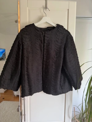 Kappa  - Säljer en svart kappa med strukturerat mönster och vida ärmar.