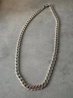 Silver 925 pansarkedja 47g - Snyggt halsband med breda, platta länkar i silverfärgad metall. Kedjan har en klassisk design och känns både stilren och trendig. Perfekt för att lyfta vilken outfit som helst med en cool touch. Pris går att diskutera vid snabbaffär