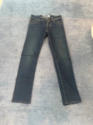 Mörkblå slim fit jeans från jacob cohen modell nick - Säljer ett par mörkblå slim fit jeans från jacob cohen. Klassisk femficksmodell med raka ben och snygga kontrastsömmar. Jeansen har en läderpatch bak i midjan och är tillverkade i mjuk denim med lite stretch för extra komfort.