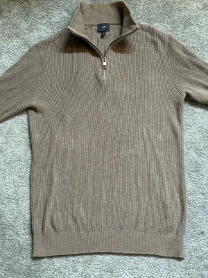 Halv Zip Slim fit - Stickad tröja från H&M i beige färg med ribbad struktur och halv dragkedja vid halsen. Tröjan har hög krage och lång ärm, perfekt för lager på lager. Enkel och stilren design som passar till det mesta.