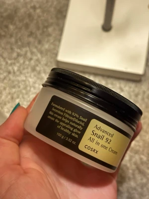COSRX - All in One Cream -  Advanced Snail 92  - En multifunktionell ansiktskräm från COSRX med 92% snigelsekretfiltrat. Krämen kommer i en rund, vit plastburk med svart lock och rymmer 100 g. Perfekt för dig som vill ha återfuktad och glowig hud, tyvärr upptäckte jag att detta ej passade min hud och därav har den påriktigt endast använts 1gång! (Dessutom med skeden som ingick -& den är slängd) 