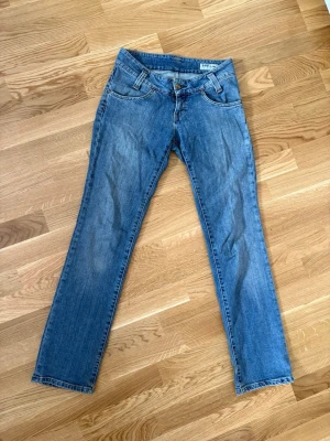 Blå straightleg jeans från Lee - Säljer ett par klassiska blå jeans från Lee med rak passform och normal midja. Jeansen har fem fickor, bälteshällor och stängs med knapp och dragkedja. Tillverkade i slitstark denim som ger en tidlös look.