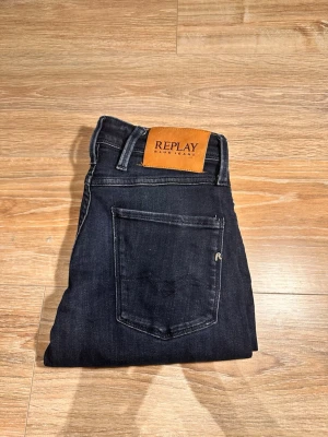 Mörkblå jeans från Replay - Snygga mörkblå jeans från Replay med klassisk femficksdesign och diskreta slitningar. Jeansen har raka ben och en skinnpatch med Replay-logga bak i midjan. Perfekta till en avslappnad och trendig stil.