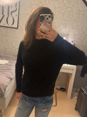 Svart stickad tröja - En enkel och stilren svart stickad tröja med rund hals och långa ärmar. Passar perfekt till jeans eller kjol och är ett måste i garderoben för dig som gillar basic plagg. Materialet ser mjukt och bekvämt ut, perfekt för kyligare dagar.