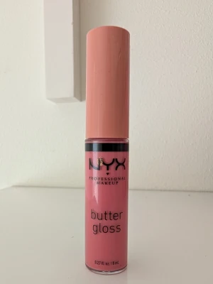 NYX Butter Gloss Creme Brulee  - Använd en gång. NYX Butter Gloss är ett läppglans i en mjuk rosa färg som ger en glansig finish. Förpackningen är cylinderformad med matchande rosa lock och transparent kropp så du ser färgen. Enkel att applicera med applikator och perfekt för dig som vill ha glansiga läppar.
