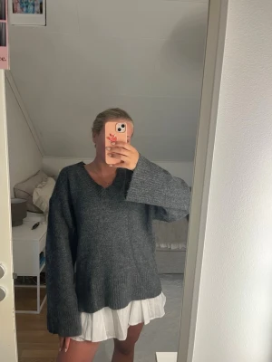 Mörkgrå oversized stickad tröja - Mysig mörkgrå stickad tröja med v-ringning och långa, vida ärmar. Tröjan har en oversize passform, från ginatricot och använd några gånger men inga defekter. 
