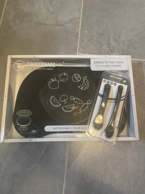 Twistshake sugmatta och tallrikset - Säljer ett svart Twistshake set med sugmatta, tallrik med lock och två skedar. Perfekt för småbarn, mattan håller tallriken på plats och motiv av frukter och grönsaker gör det roligare vid måltiden. Allt är i plast och designat för att underlätta matstunden.
