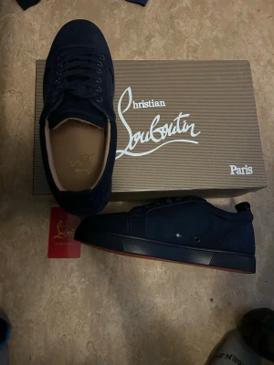Mörkblå sneakers Christian Louboutin - Snygga mörkblå sneakers från Christian Louboutin i mocka med klassisk röd sula och diskret logga på hälen. Skorna har lågt skaft, svarta snören och en stilren design som passar till det mesta. Levereras med originalkartong och certifikat.