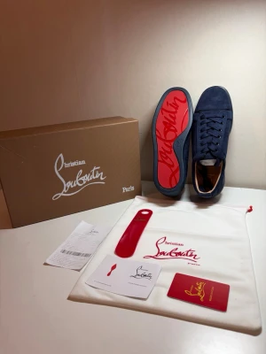 Marinblå sneakers från Christian Louboutin - Snygga marinblå sneakers från Christian Louboutin i mocka med klassisk röd sula och matchande blå snörning. Skorna har en låg profil och exklusiv känsla, perfekt för dig som vill sticka ut med stil. Kommer med originalkartong, dustbag och tillbehör.
