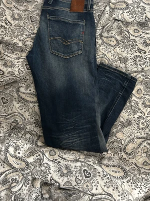 Mörkblå jeans från Replay - Säljer ett par mörkblå jeans från Replay med snygga slitningar och klassisk femficksmodell. Jeansen har en rak passform och detaljerade sömmar på bakfickorna. Perfekta för dig som gillar en avslappnad men stilren look. Storlek 31 i midja 30 i längd alltså 31:30. Säljer då jag ej gillsr hur de sitter på mig, är på riktigt i nyskick då de är knappt använda alls, kanske max 10 gånger. Köpta för 1600 kr nya, säljer för 549 som startpris. Priset kan såklart stt diskutera! BVSA!!