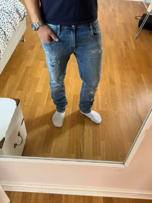 Blå slitna slim fit jeans - Säljer ett par ljusblå slim fit jeans med slitningar och detaljer på låret och knät. Jeansen har klassisk femficksmodell och normal midja. Perfekta för en avslappnad och trendig look. Passar dig runt 180, skick 9/10