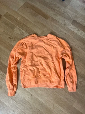 Orange sweatshirt i storlek XS - En enkel och snygg orange sweatshirt med rund hals och långa ärmar. Tröjan har ribbade muddar vid ärmslut och nederkant. Perfekt för en avslappnad och trendig look. Tillverkad i mjukt material för extra komfort.