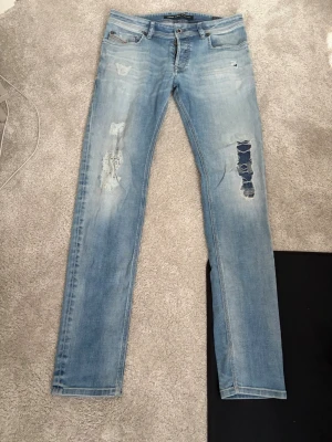 Diesel jeans - Säljer ett par ljusblå jeans med raka ben och slitningar på framsidan. Jeansen har klassisk femficksdesign och detaljerade slitningar på båda benen för en trendig look. Perfekta för dig som gillar en avslappnad och cool stil. Med snygg tvätt. 