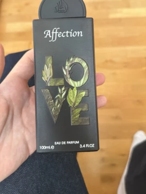 Affection Love Eau de Parfum 100ml - Parfymflaska med svart, rektangulär design och texten 'Affection' samt 'LOVE' i stora bokstäver dekorerade med bladmotiv. Innehåller 100 ml Eau de Parfum. Modern och stilren look som passar dig som gillar unika detaljer.