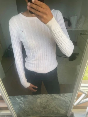 Vit kabelstickad tröja - Snygg vit kabelstickad tröja med rund hals och långa ärmar. Tröjan har ett klassiskt mönster och sitter figurnära. Perfekt att matcha med jeans eller kjol för en clean look.