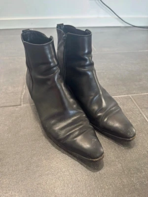 Svarta skinnstövletter med dragkedja - Säljer ett par svarta stövletter i skinn med spetsig tå och dragkedja på sidan. Klassisk och stilren modell som passar till många olika outfits. Perfekta för dig som gillar en edgy och tidlös look.
