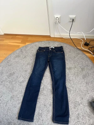 Mörkblå raka jeans - Säljer ett par mörkblå jeans med rak passform och klassiska fem fickor. Jeansen har orange sömmar och knappgylf. Perfekta till en avslappnad stil och funkar året runt.