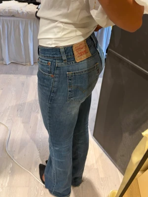 Blå jeans från Levi's - Intressebolag på ett par vintage blå jeans från Levi's med rak passform och normal midja. Jeansen har fem fickor, synliga sömmar och en ikonisk läderpatch bak i linningen. Jag är 170 cm o brukar ha 36/s i byxor, sitter perfekt 