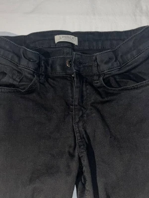 Svarta jeans från Lindex - Snygga svarta jeans från Lindex med fickor och normal midja. Jeansen har bälteshällor och dragkedjegylf. Materialet är mjukt och stretchigt för en bekväm passform🩷Jeansmodell: Freja
