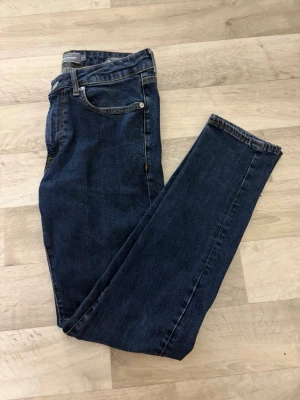 Mörkblå slim fit jeans W32/L32 - Snygga mörkblå slim fit jeans med klassisk femficksdesign och smal passform. Jeansen har normal midja och är tillverkade i stretchigt denimtyg för extra komfort. Perfekta för en avslappnad och trendig look.