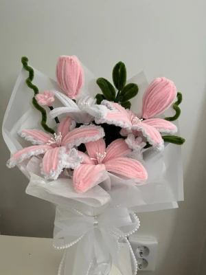 Handgjord bukett av garnblommor - Unik bukett med handgjorda blommor i rosa och vitt garn, inslag av gröna blad och stjälkar. Blommorna är formade som liljor och knoppar, inslagna i vitt papper och dekorerad med pärlband och rosett. Perfekt som dekoration eller present.