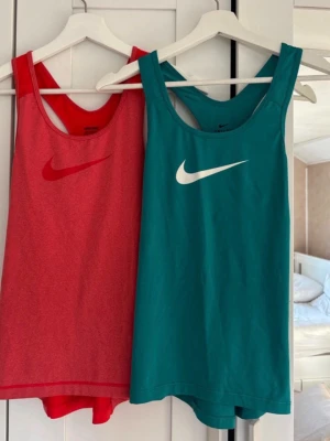 Nike träningslinnen orange & turkos - Två snygga träningslinnen från Nike, ett i orange med röd logga och ett i turkos med vit logga. Båda har brottarrygg och är tillverkade i ett lätt och snabbtorkande material.                                Obs. Det turkosa linnet har en liten tråd som börjat gå upp, se sista bilden! 