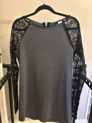 Grå topp med spetsärmar från H&M - Snygg grå topp från H&M:s Divided-kollektion med långärmade spetsdetaljer i svart. Toppen har rund halsringning och en rak passform. Perfekt för dig som gillar en mix av basic och coola detaljer.