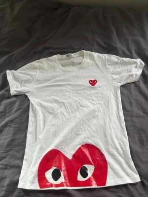 Vit t-shirt med rött hjärtmotiv - Vit t-shirt med korta ärmar och ett stort rött hjärta med ögon tryckt längst ner samt ett mindre hjärta på bröstet. T-shirten har en klassisk passform och är tillverkad i mjuk bomull. Perfekt för dig som gillar grafiska tryck och vill sticka ut.