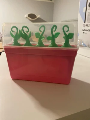 Baby Born Surprise Baby Planter - Detta set innehåller en Baby Born Surprise Baby Planter med en rosa blomlåda, fem gröna växtskal och Baby Born Surprise-dockor. Tillbehör som en liten säng, en vagga och ett badkar ingår också.