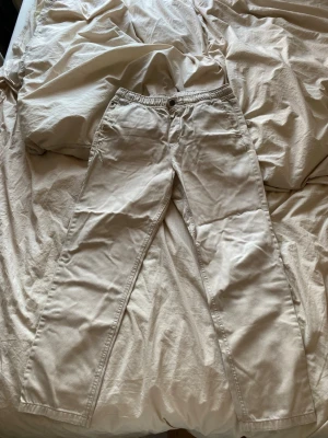 Beiga chinos med resårmidja - Säljer ett par beiga chinos med avslappnad passform och resår i midjan. Byxorna har sidofickor fram och en bakficka med liten patch. Perfekta för en chill och enkel stil. Materialet känns mjukt och bekvämt.