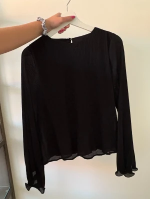 Svart blus med vida ärmar - Snygg svart blus med diskreta ränder. Blusen har långa, vida ärmar och vågig kant nertill samt vid ärmslut. 