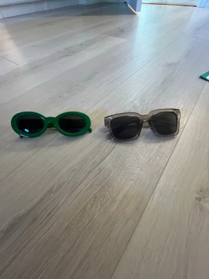 Två par solglasögon - Säljer två par solglasögon: ett par med gröna, ovala bågar och mörka glas samt ett par med fyrkantiga bågar och svarta glas. Mycket bra skick. Kan köpas var för sig